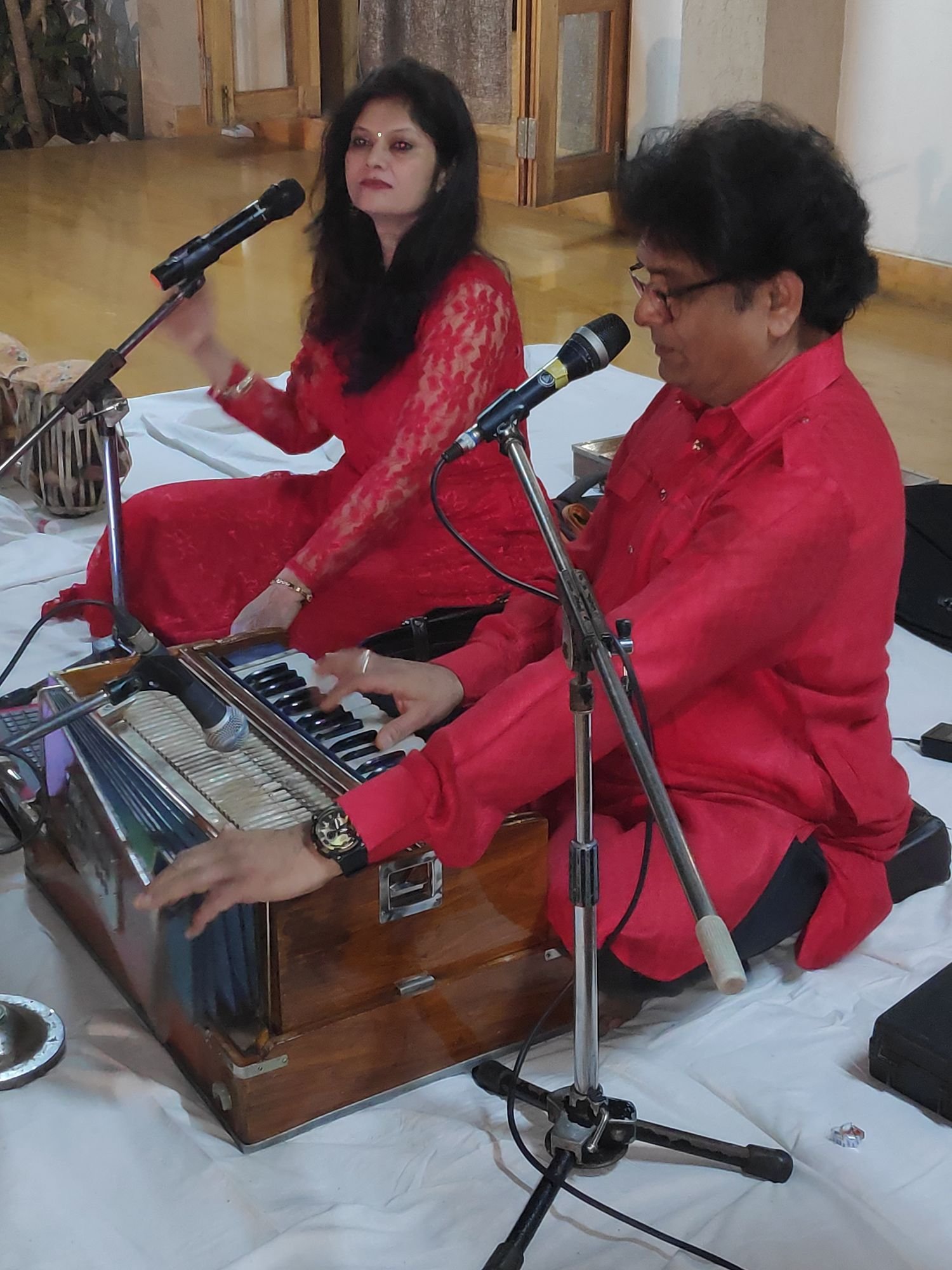 Sanjay and Sanjyot Banubakode in red, seated at the harmonium on white sheets
