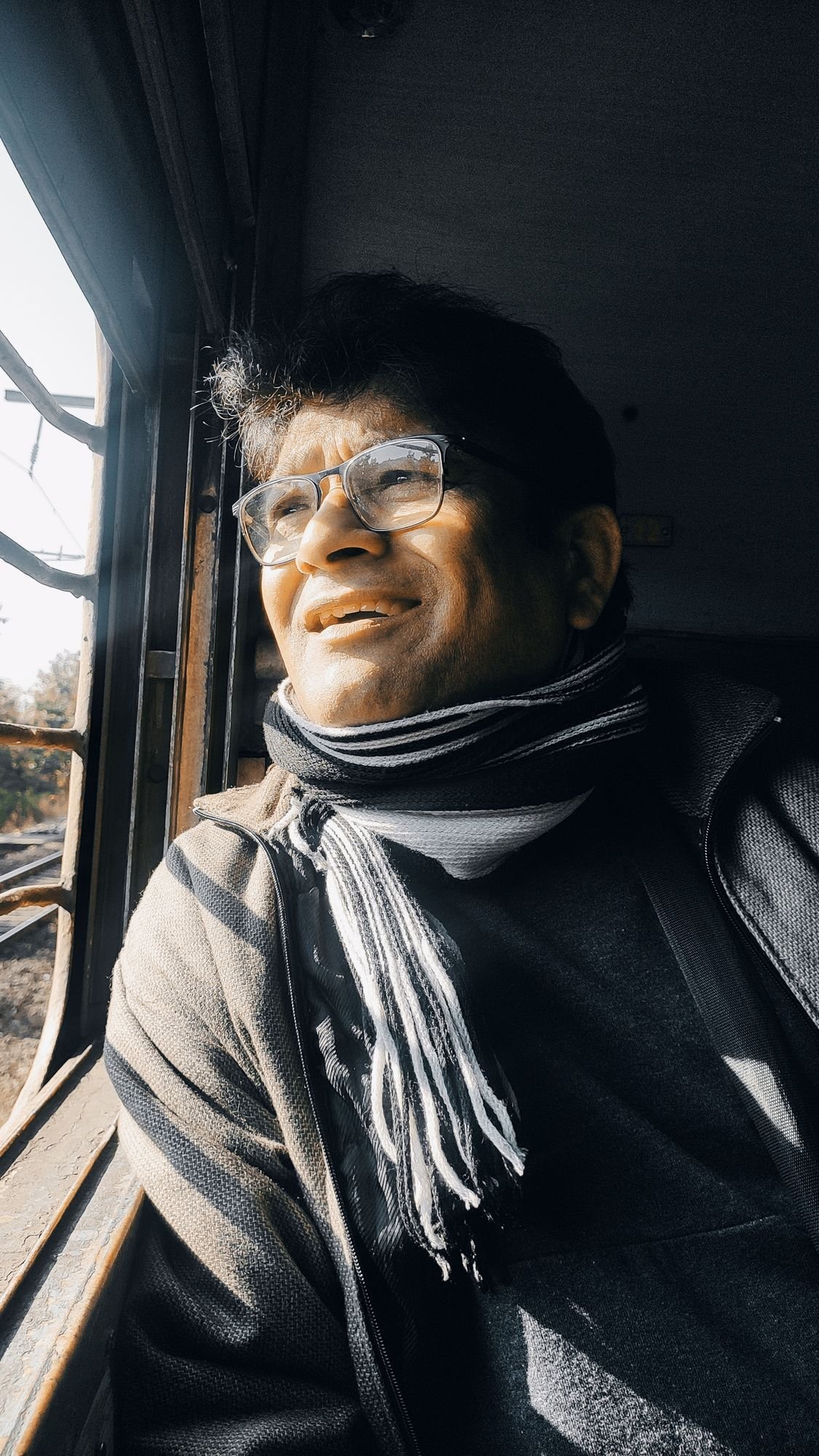 Black-and-white portrait of Sanjay Banubakode by a window, wearing a scarf, smiling toward the light