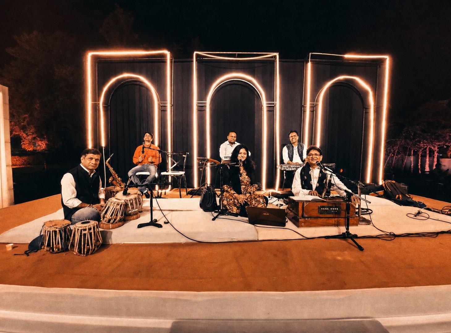 Night concert beneath three illuminated arches, Sanjay Banubakode at the harmonium with the ensemble