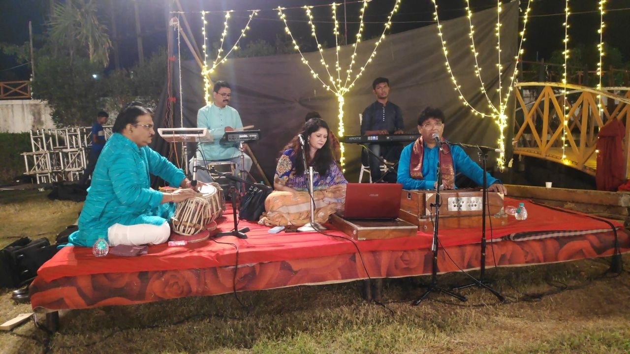 Outdoor stage draped in fairy lights, ensemble seated on red