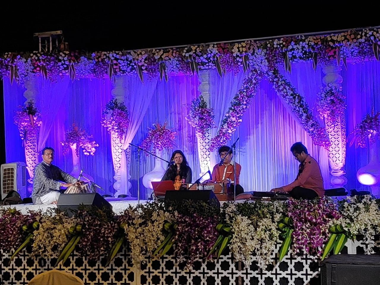 Ensemble on a stage framed by white flowers and purple light