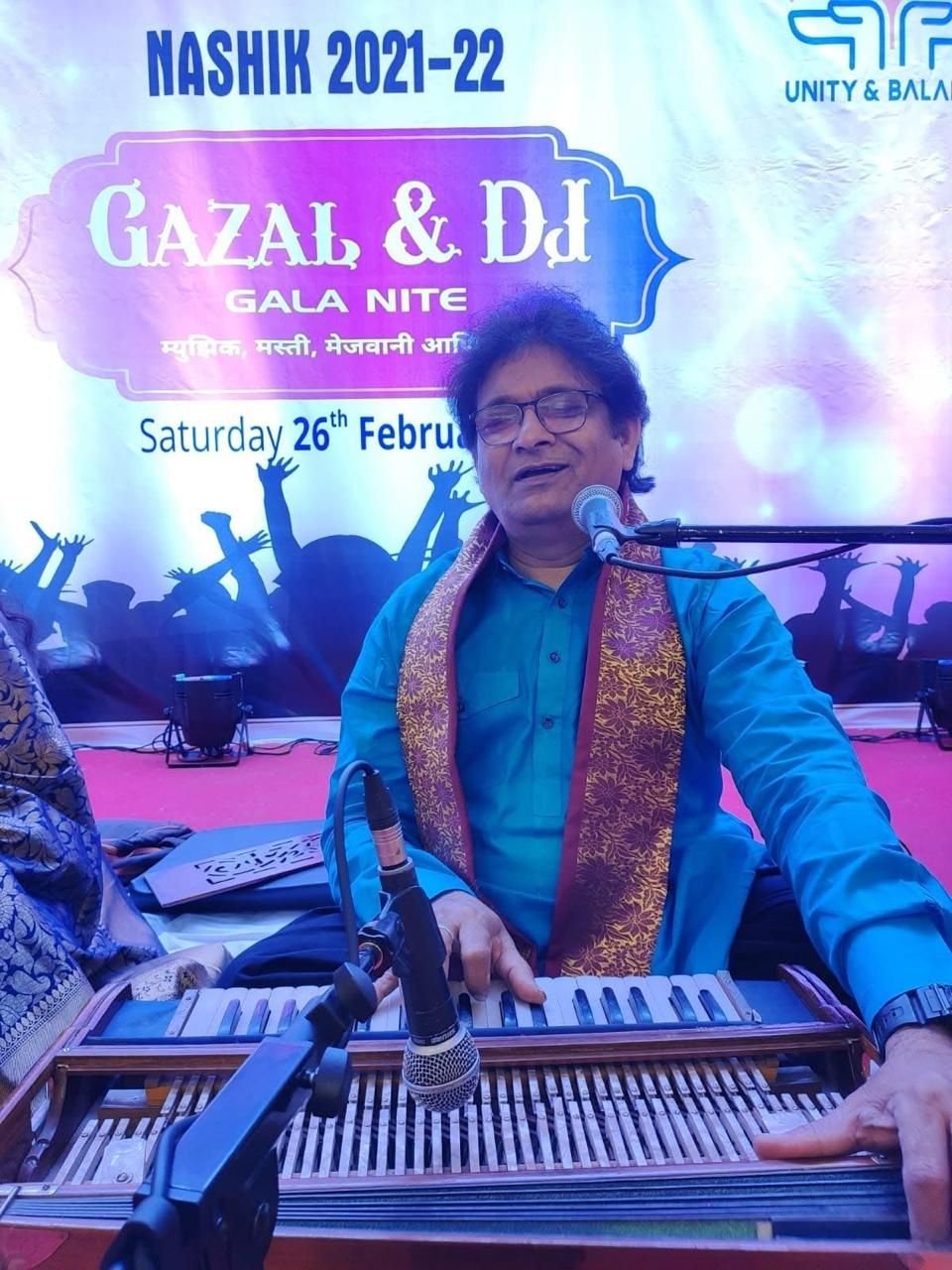 Sanjay Banubakode singing at the harmonium with a golden stole, IMA Nashik gala