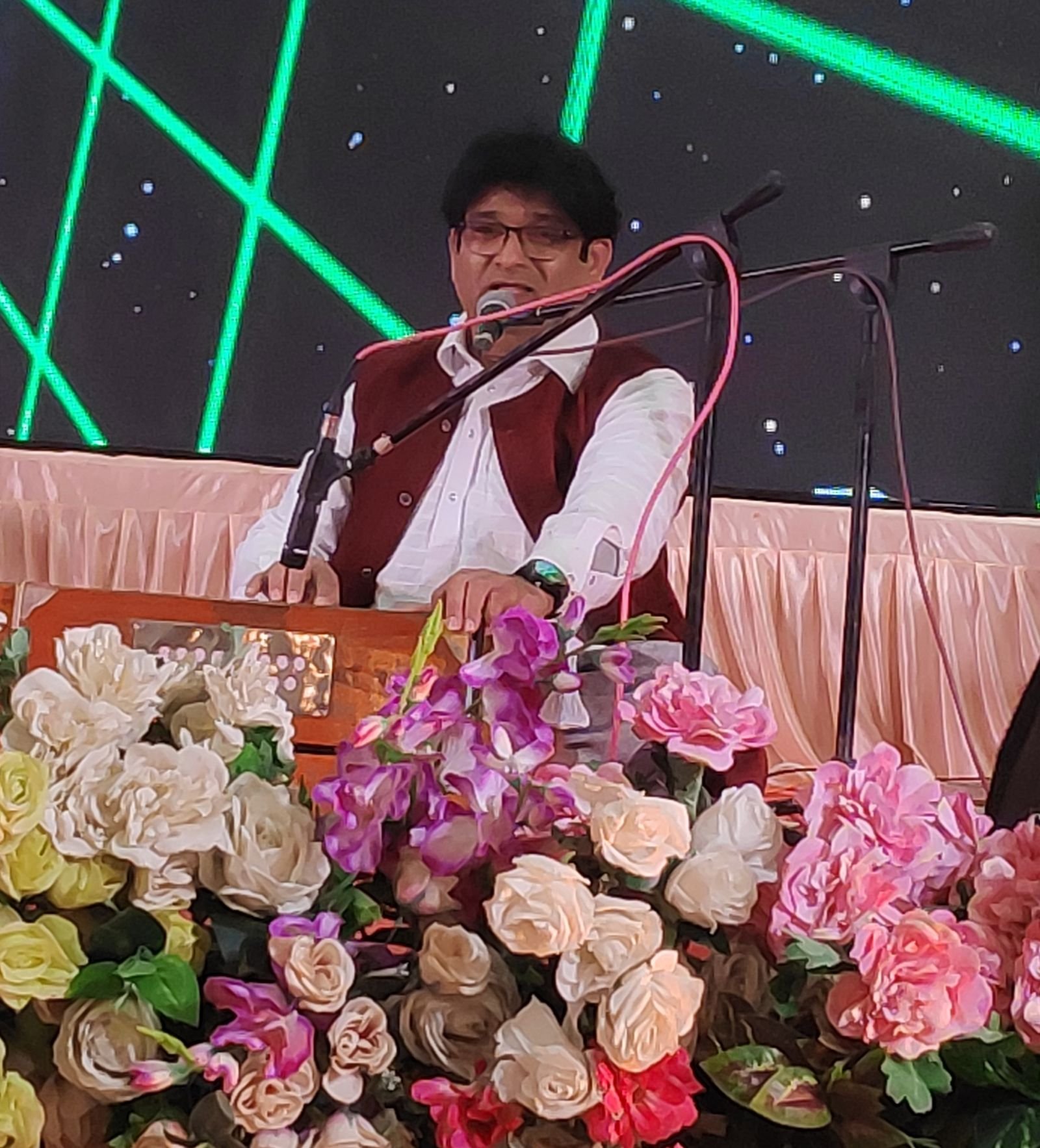 Sanjay Banubakode at the harmonium in front of a starry LED wall and roses