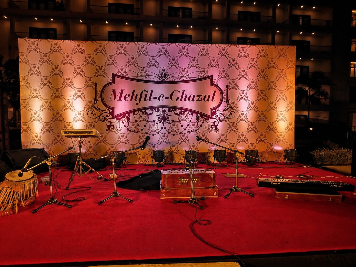 An empty Mehfil-e-Ghazal stage: harmonium, tabla and microphones set on a red carpet before the audience arrives