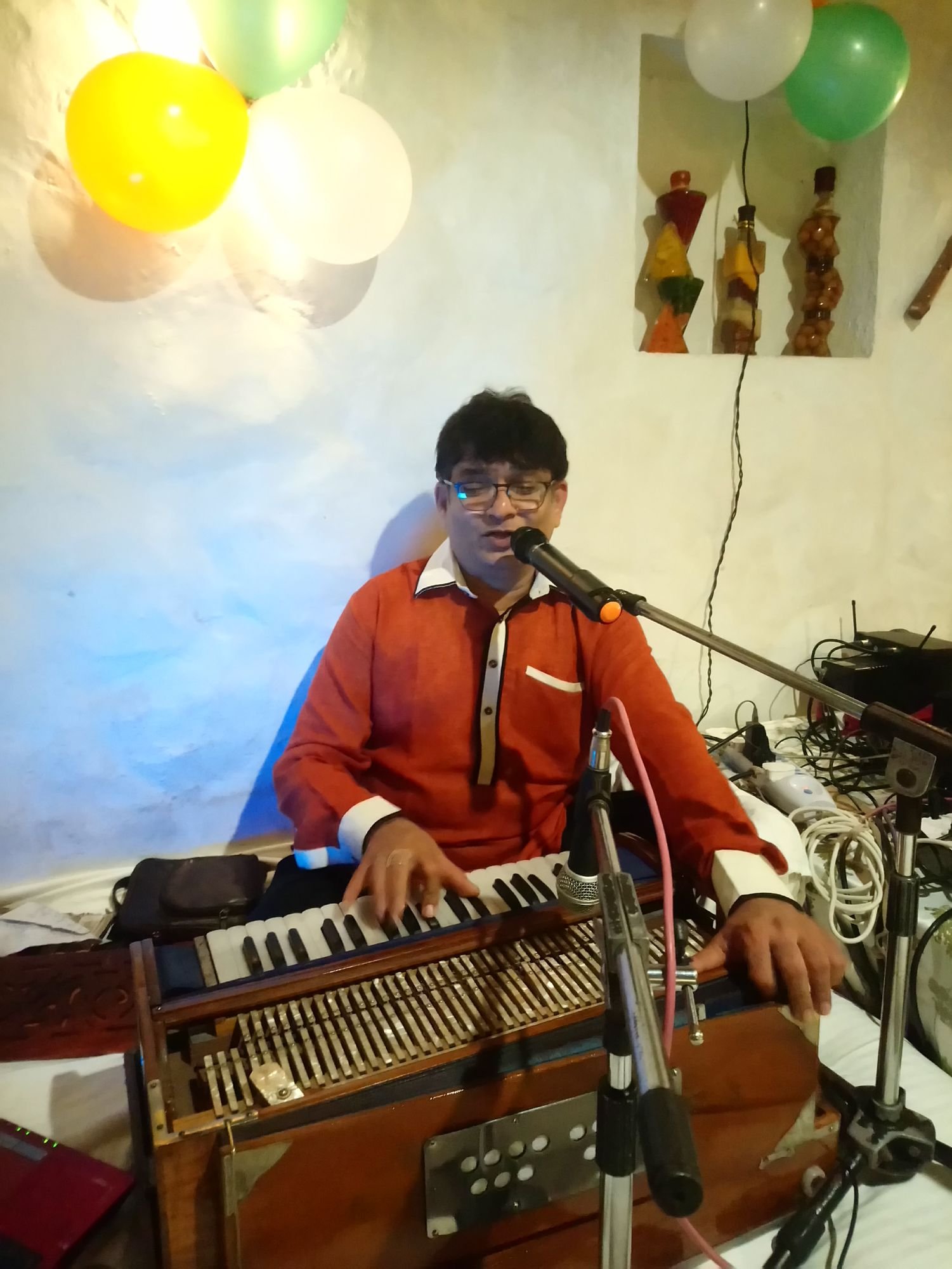 Sanjay Banubakode in an orange shirt at the harmonium, balloons above