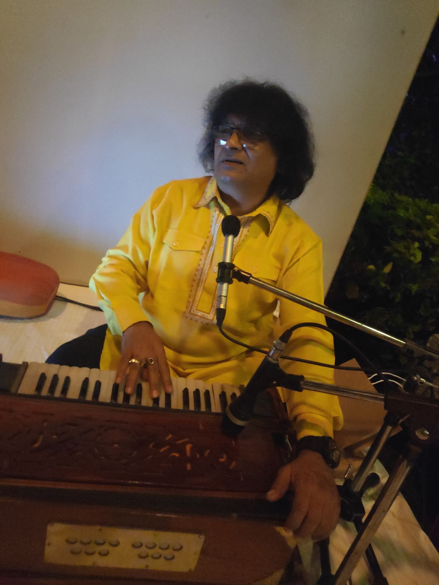 Sanjay Banubakode in a yellow kurta singing at the harmonium